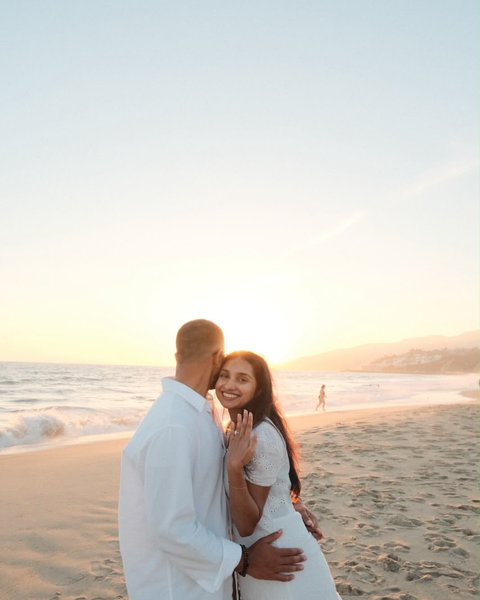 A couple dressed in white embracing on the beach at sunset